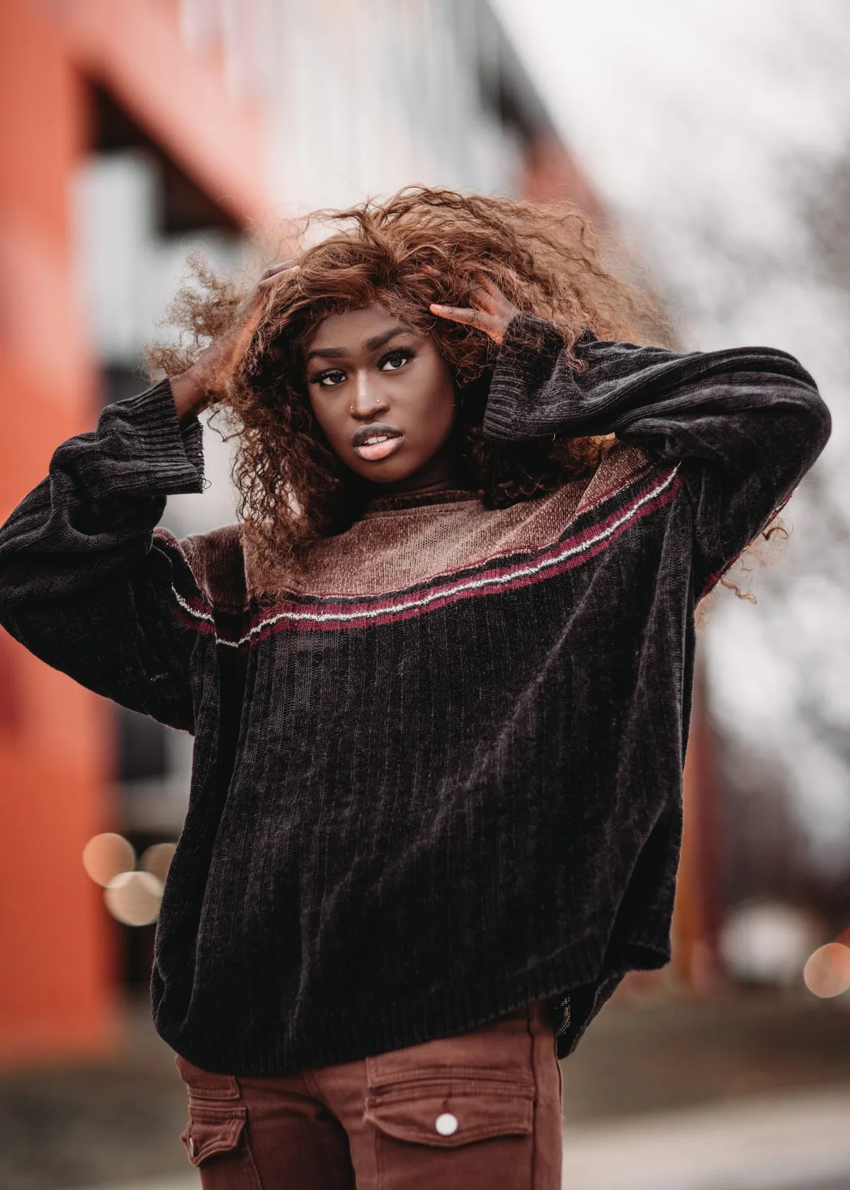 A woman in a textured brown sweater standing in an urban setting.