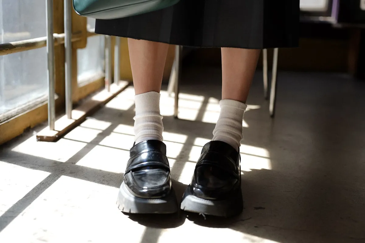 Black loafers and white socks worn in a sunlit indoor setting.