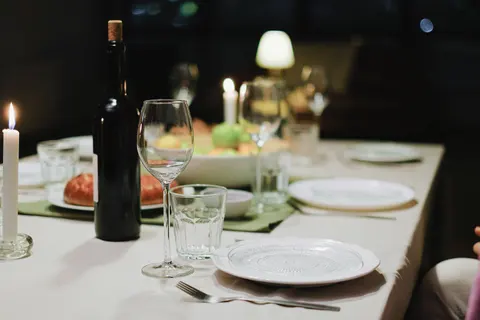 A dinner table set with plates, wine glasses, food and candles.