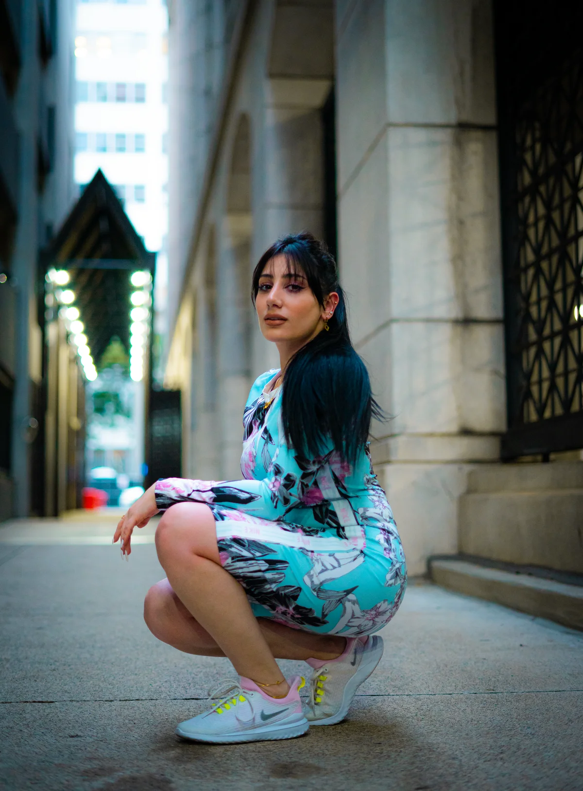 A woman wearing a colorful dress and sneakers in an urban alley.