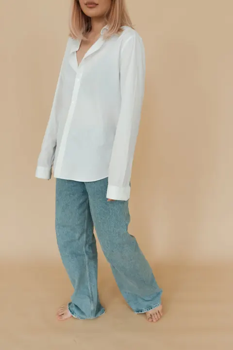 A woman wearing a white shirt and blue jeans outdoors.